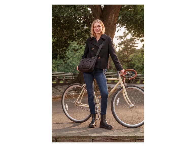 Frau in schwarzer Jacke und Jeans, steht neben einem Fahrrad mit Umhängetasche.