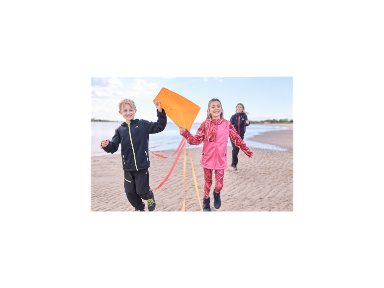 Kinder laufen mit einem Drachen am Strand, gekleidet in CRIVIT Funktionstights.