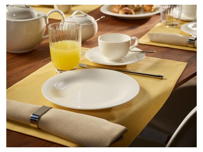 Frühstückstisch mit weißen Tellern, Tassen, Kanne, Saftglas und Servietten.
