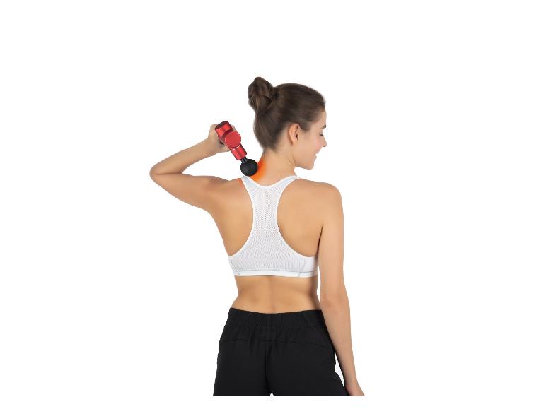 Eine Frau in Sportkleidung verwendet eine Massagepistole auf ihrem Rücken.