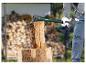 Person spaltet Holz mit einer Spaltaxt, mit einem Holzstapel im Hintergrund.