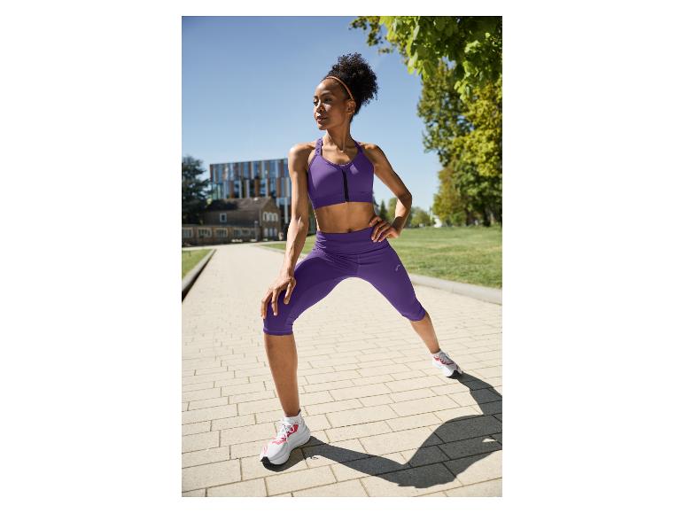Frau in lila Sport-BH und Capri-Leggings dehnt sich draußen.