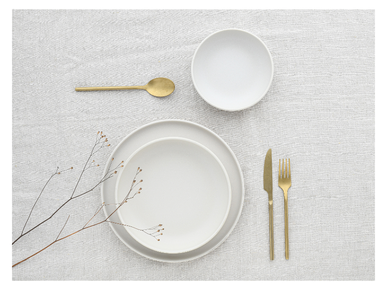 Weißes Geschirr, goldenes Besteck und minimalistische Dekoration.