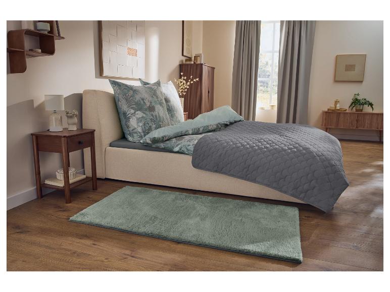 Schlafzimmer mit Bett, floraler Bettwäsche, grauer Decke, Nachttisch und grünem Teppich.