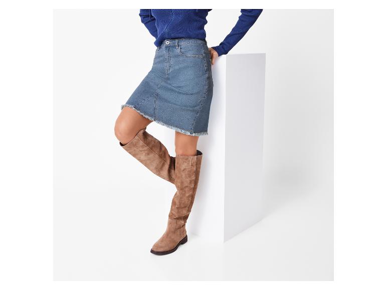 Frau in blauem Pullover und Jeansrock, braunen hohen Stiefeln.