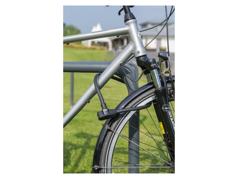 Silbernes Fahrrad mit schwarzem Schloss an einem grauen Ständer auf grünem Gras.