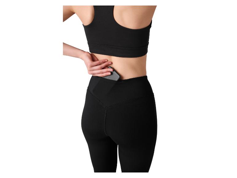 Frau in schwarzem Sport-BH und Leggings mit Handy in der Tasche