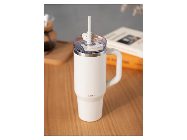 Weißer Bodum Reisebecher mit Henkel und Strohhalm auf Holztisch.