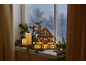 Beleuchtetes Weihnachtshaus aus Holz auf einer Fensterbank mit Kerzen und Tannenzweigen