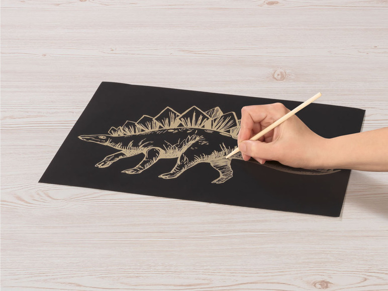 Eine Hand zeichnet einen goldenen Dinosaurier auf schwarzem Papier.