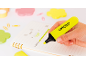 Hand markiert Text in Notizbuch mit gelbem Textmarker, umgeben von Büromaterial.