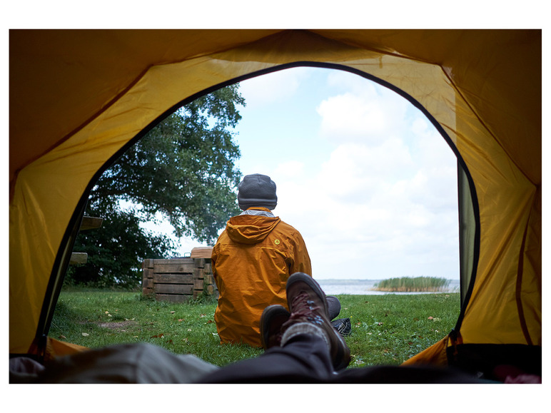 Eine Person sitzt in einem gelben Zelt und schaut auf einen See.