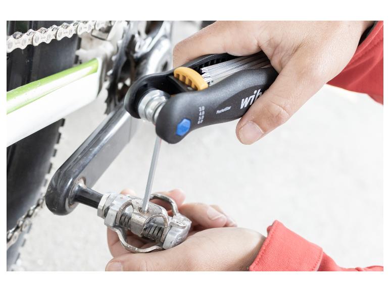 Hände stellen ein Fahrradpedal mit einem Multifunktionswerkzeug ein.
