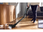 Person saugt Boden mit kabellosem Staubsauger in hellem Wohnzimmer.