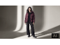 Frau in weinroter Daunenjacke, schwarzem Pullover, weiter Hose und Stiefeln.