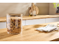 Vorratsglas mit Holzdeckel gefüllt mit Granola auf einer Holz-Arbeitsplatte.