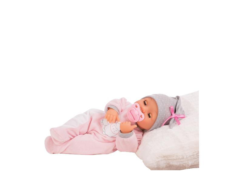 Babypuppe in rosa Strampler mit Mütze und Schnuller, auf einem weißen Kissen liegend.