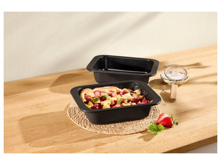 Zwei schwarze Backformen, eine mit Obstcrumble, auf einem Holztisch mit Erdbeeren.