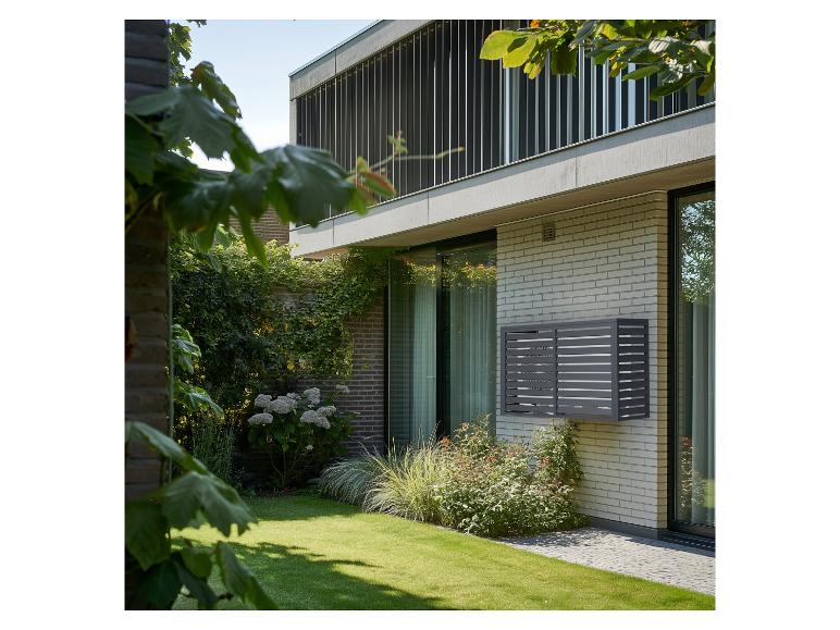 Graues Außengerät einer Klimaanlage an einer hellen Ziegelwand eines modernen Hauses mit Garten.