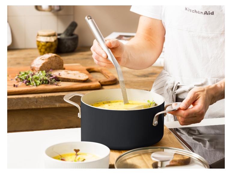 Eine Person schöpft Suppe aus einem KitchenAid Topf mit einer Kelle.