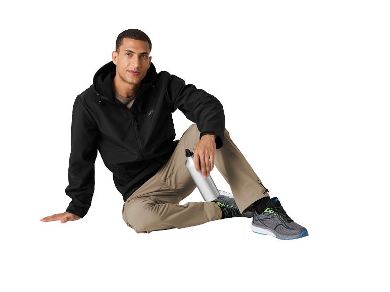 Mann in schwarzer Jacke, khakifarbener Hose und Sportschuhen, hält eine Wasserflasche.