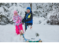 Zwei Kinder in Winterkleidung mit Schlitten und kleinem Schneemann in verschneiter Landschaft.