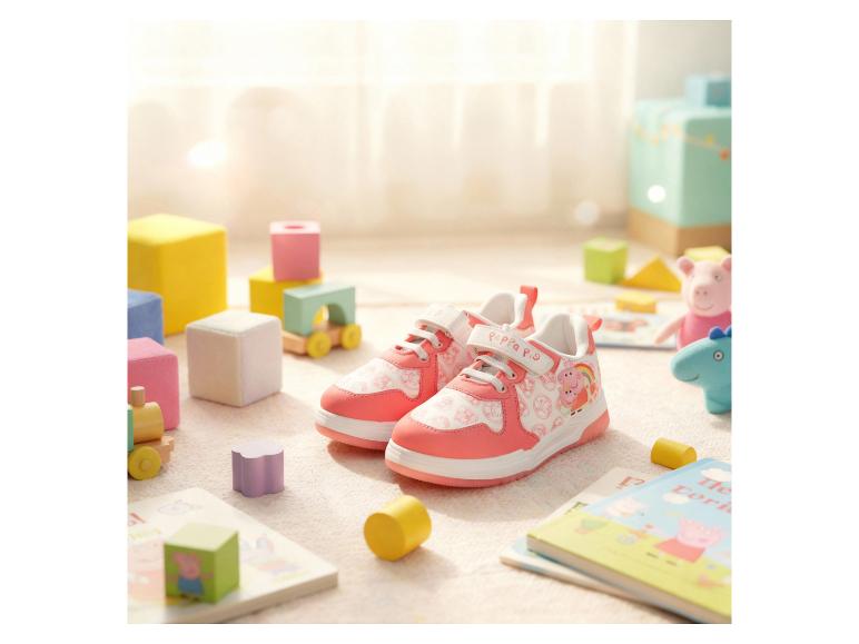 Rosa Kinderschuhe mit Zeichentrickfiguren, umgeben von Spielzeug und Büchern.