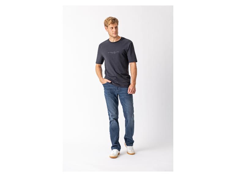 Mann in dunkelblauem T-Shirt mit Schriftzug und blauen Jeans, weiße Sneaker.