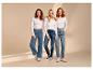 Drei Frauen tragen weiße Langarmshirts und Jeans, posieren vor beigem Hintergrund.