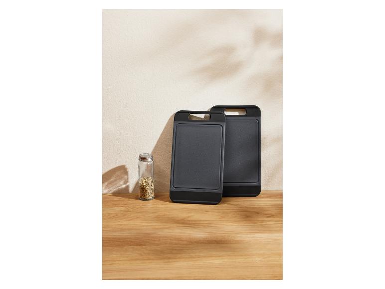 Zwei schwarze Schneidebretter und ein Gewürzglas auf einem Holztisch.