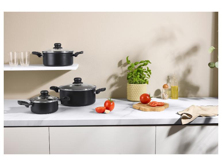 Schwarze Kochtöpfe mit Glasdeckeln, frische Tomaten, Basilikum und Küchenaccessoires.