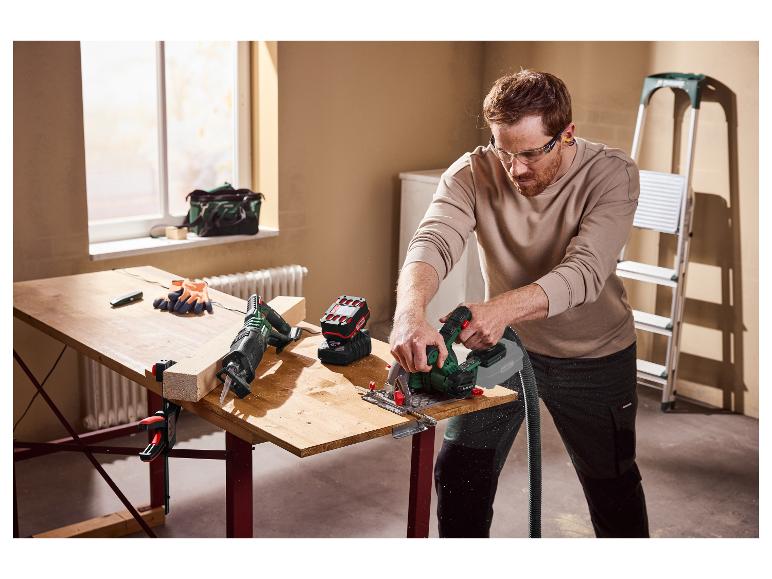 Mann sägt ein Holzbrett mit einer Kreissäge und trägt dabei eine Schutzbrille.