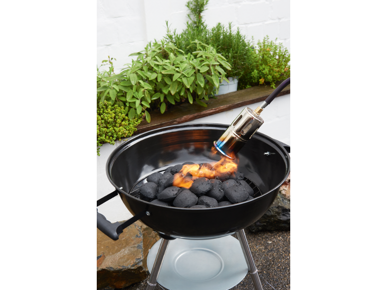 Holzkohlegrill mit Anzündhilfe, umgeben von Kräuterpflanzen.