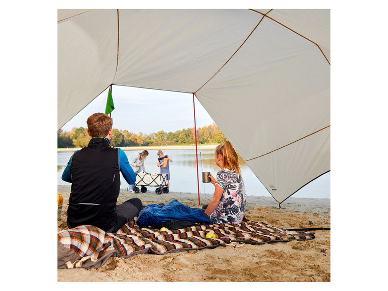 Eine Familie genießt ein Picknick unter einem Zelt am Strand.