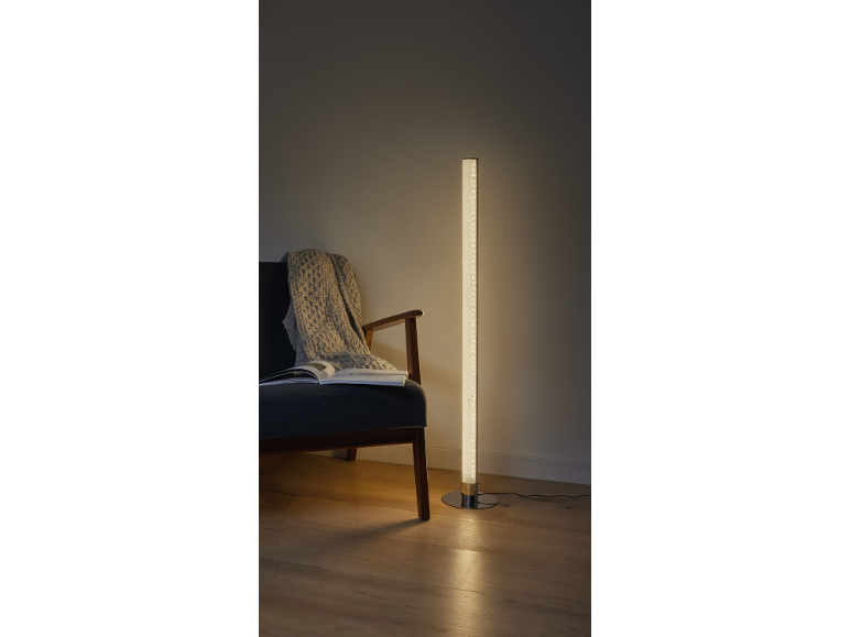 LED-Stehlampe mit Blasen neben einem Sessel mit Decke und Buch.