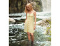 Eine Frau in einem gelben, geknöpften Sommerkleid steht in einem Fluss.