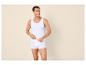 Mann in weißem Unterhemd und Boxershorts, lächelnd und zur Seite blickend.