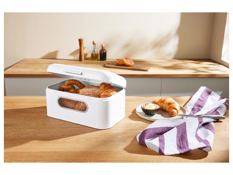 Weiße Brotbox voller Backwaren auf einem Holztisch, mit einem Croissant und Butter.