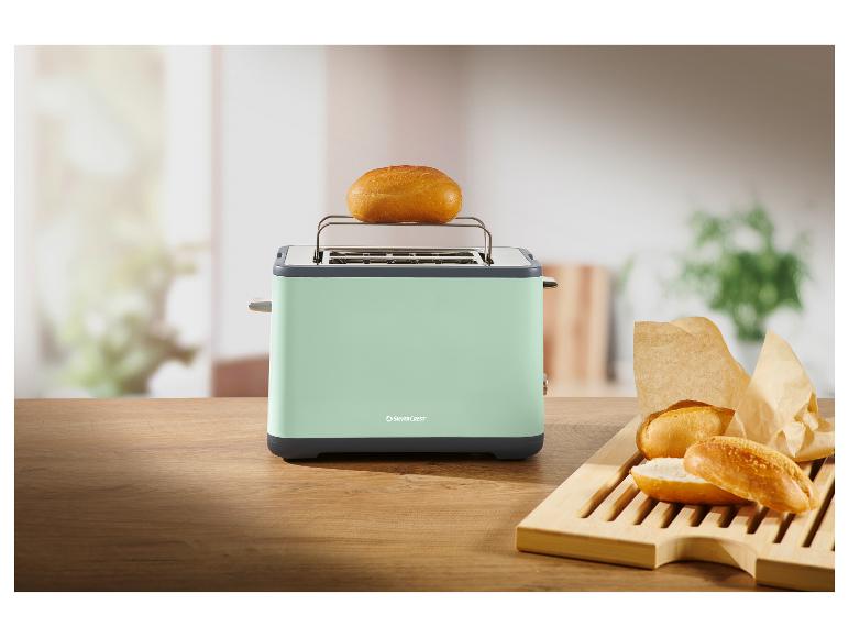 Minzgrüner Toaster mit einem Brötchen darauf und weiteren Brötchen auf einem Holzbrett.