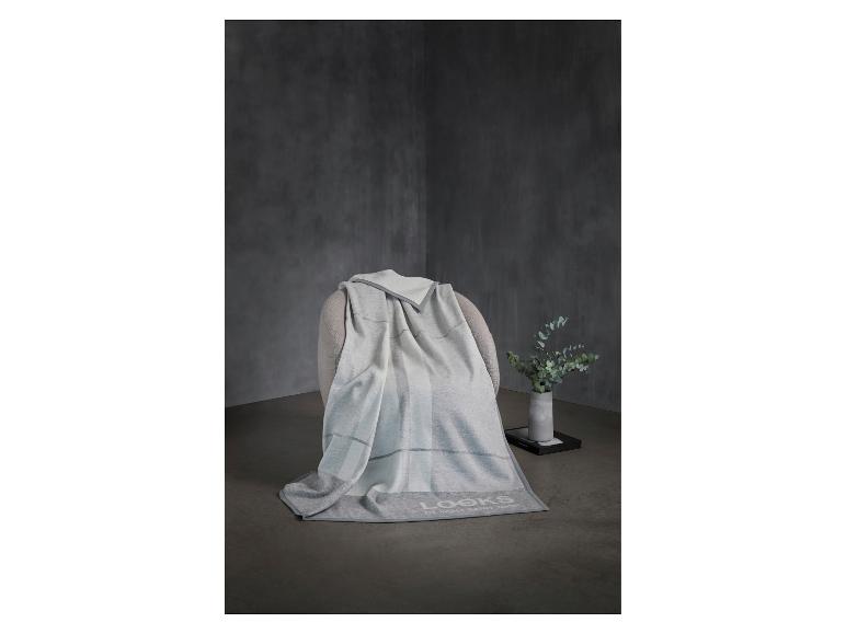 Grau-weiße Decke auf einem Sessel, daneben eine Vase mit Grünzeug.