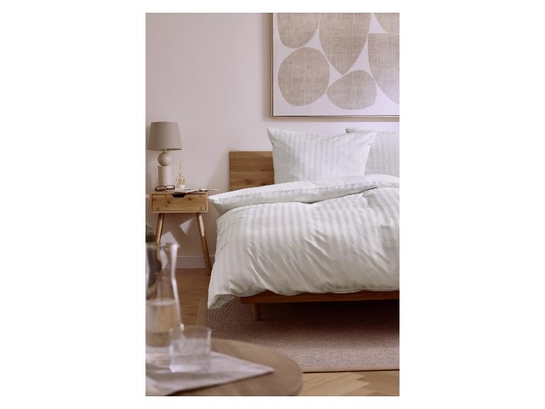 Bett mit weiß gestreifter Bettdecke und Kissen, Nachttisch aus Holz mit Lampe und Dekoration.