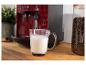 Kaffeemaschine schäumt Milch in eine Glastasse, daneben ein Glas mit Kaffeebohnen.