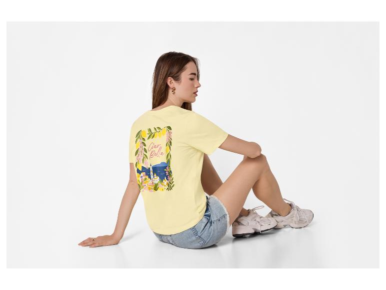 Frau in gelbem T-Shirt mit „Ciao Bella“-Aufdruck und Jeans-Shorts, auf dem Boden sitzend.