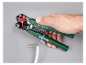 Hand hält automatische Abisolierzange, isoliert ein blaues Kabel ab, mit anderen Kabeln sichtbar.