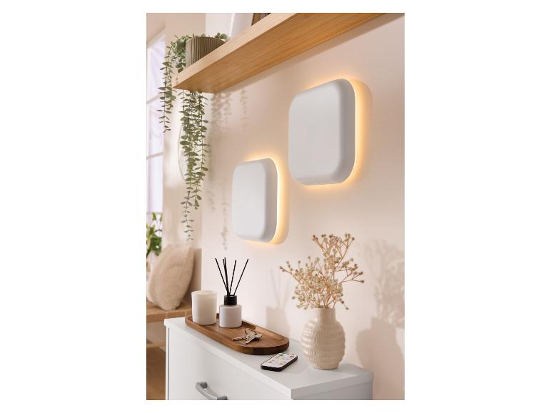 Zwei quadratische Wandleuchten mit warmem Licht über einer Kommode mit Dekoration.