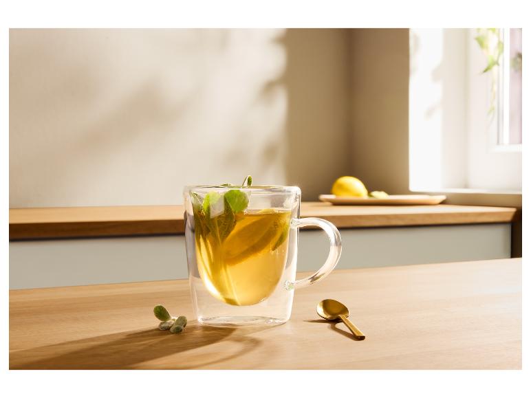 Transparentes Glas mit Tee, Zitrone und Minze auf einem Holztisch, daneben ein goldener Löffel.