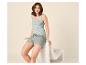Lächelnde Frau in hellgrünem Tanktop und Schlafshorts, auf einem Stuhl sitzend.