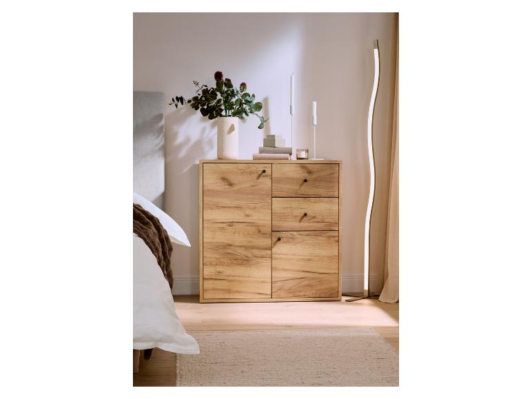 Holzkommode mit Schubladen und Türen, dekoriert mit einer Blumenvase und Kerzen, neben einem Bett.