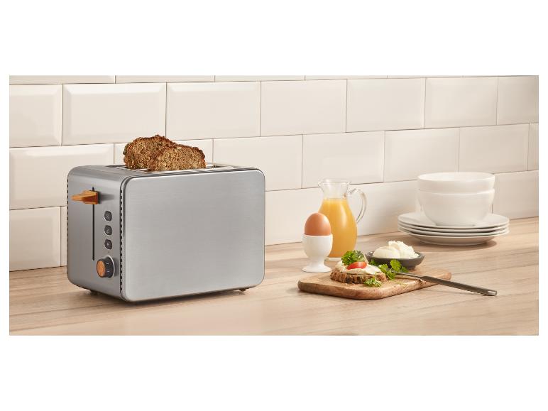 Edelstahl-Toaster mit Brot, Ei, Saft und Frischkäse auf einer Holztheke.