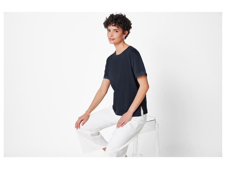 Eine Frau trägt ein dunkelblaues T-Shirt mit Spitze und eine weiße Hose.